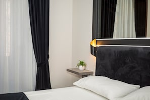 Une chambre d’hôtel moderne, équipée d’un lit, d’une table de chevet agrémentée d’une plante et d’une petite table de nuit avec une lampe.
