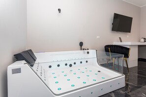 A modern spa area with a glass-enclosed hot tub, a mounted television, and a sleek black chair.