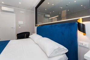 Et moderne hotelværelse med en stor seng, en sort polstret sengegavl, et hvidt natbord og en vægmonteret aircondition.