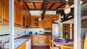 A compact kitchen with wooden cabinets, a stove, microwave, and a dining area with a table and chairs. - THE OUTDOOR ROOFTOP HOUSE (Calice Ligure)