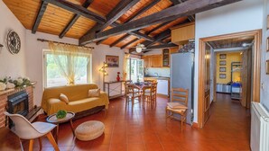 A cozy living room with a sofa, dining table, and chairs, a kitchen area with cabinets and a refrigerator, and a hallway leading to a bedroom. - THE OUTDOOR ROOFTOP HOUSE (Calice Ligure)