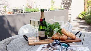 Una mesa con una botella de champán, copas, una jarra, un pan y un par de anteojos sobre una tabla de madera.