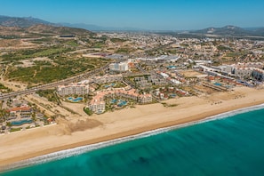 Vista aérea de una zona turística costera con hoteles frente a la playa, una playa y montañas al fondo.