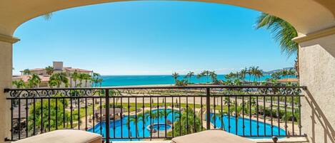 A balcony with a view of a swimming pool and the ocean.