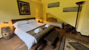 A hotel room with a large bed, a smaller bed, a wooden bench, a rug, and a painting on the wall.