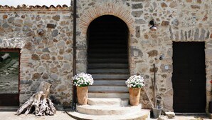 Un bâtiment en pierre doté d’une grande entrée en arc de cercle, d’une porte en bois et de deux jardinières placées sur les marches.