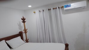 Une chambre à coucher avec un lit en bois, des rideaux blancs et un appareil de climatisation fixé au mur.