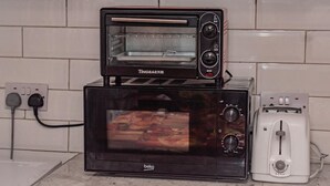 Une cuisine avec un four électrique noir et blanc et un grille-pain placés l’un sur l’autre, le tout posé sur un micro-ondes noir.