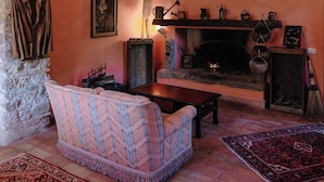 A cozy living room with a stone archway, a fireplace, a sofa, and a patterned rug. - West Way (Tolfa)