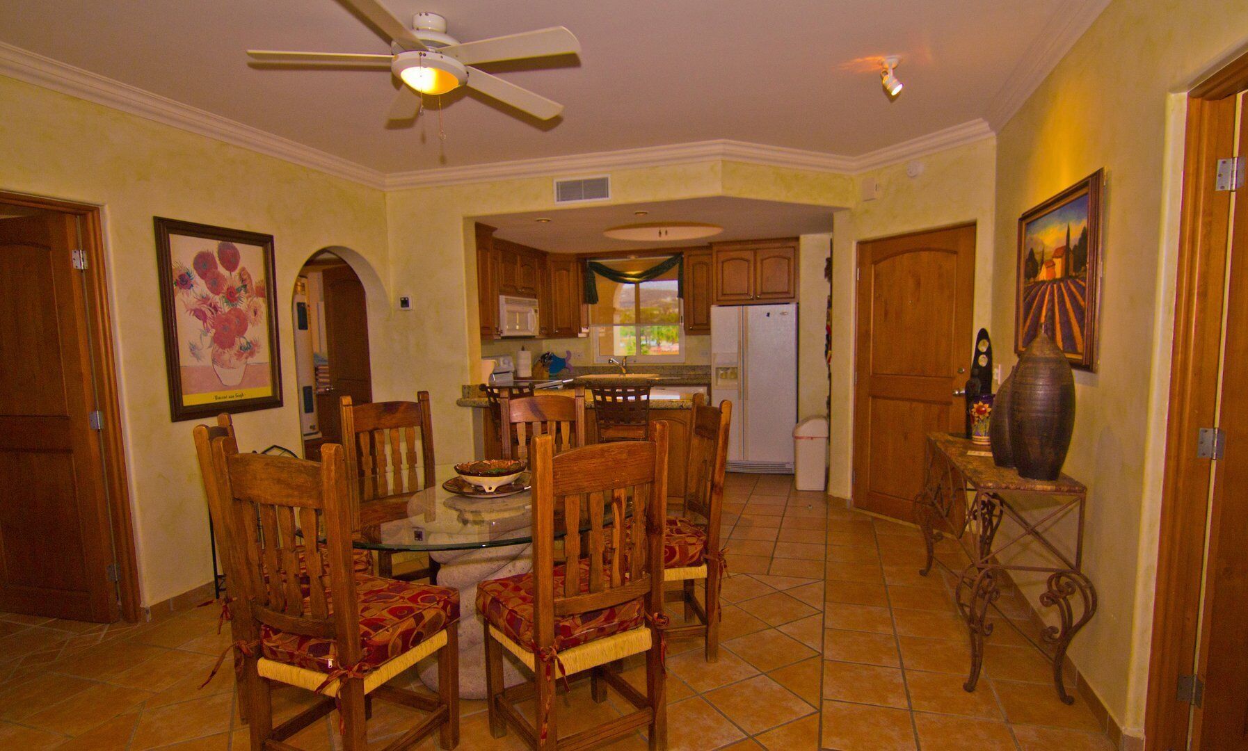 A dining area with a table and chairs, a ceiling fan, and a kitchen in the background.