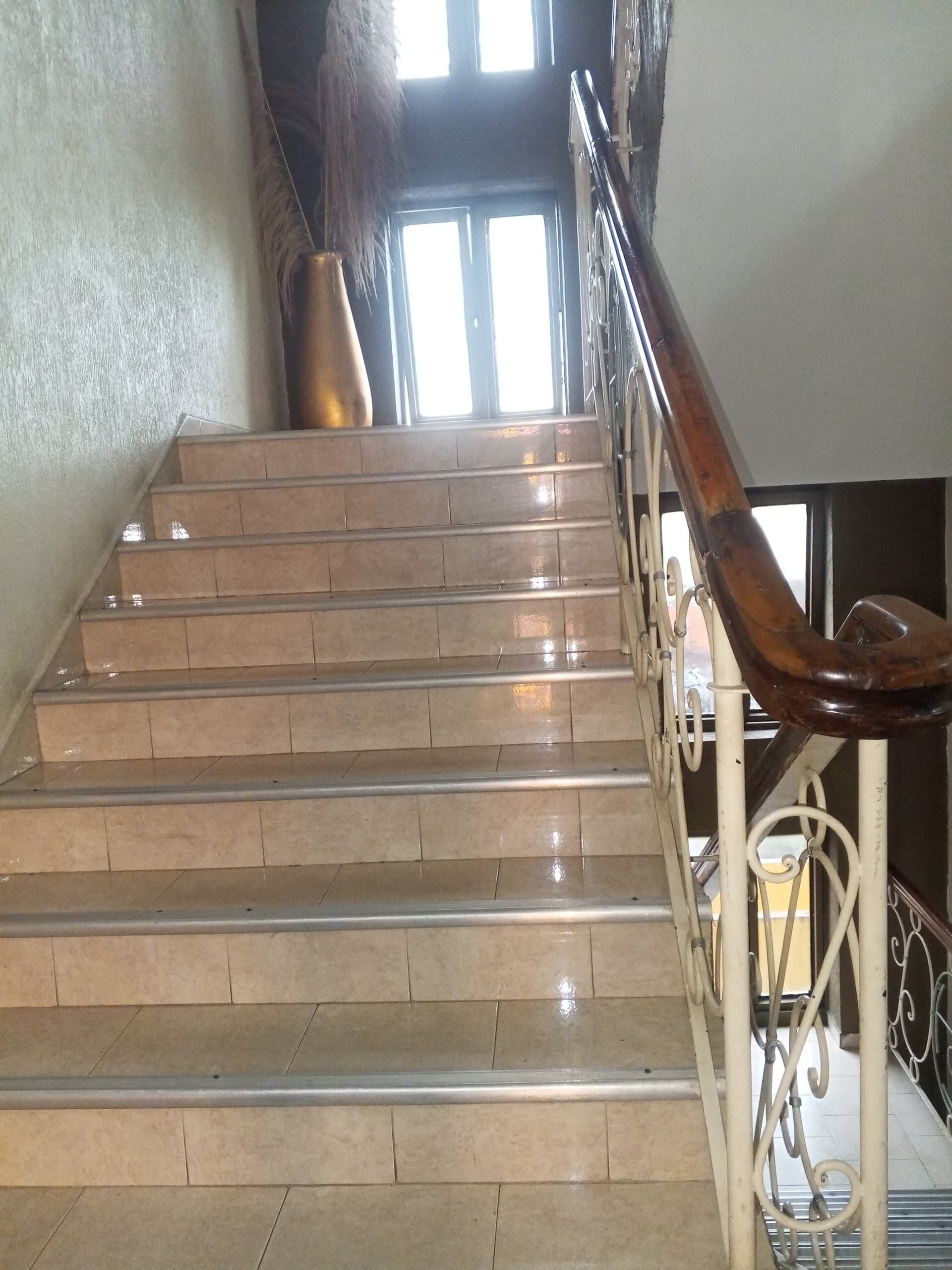 Un escalier avec une rampe métallique et un vase placé sur le palier.