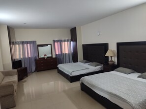 Une chambre avec deux lits, une commode, une télévision et une lampe.
