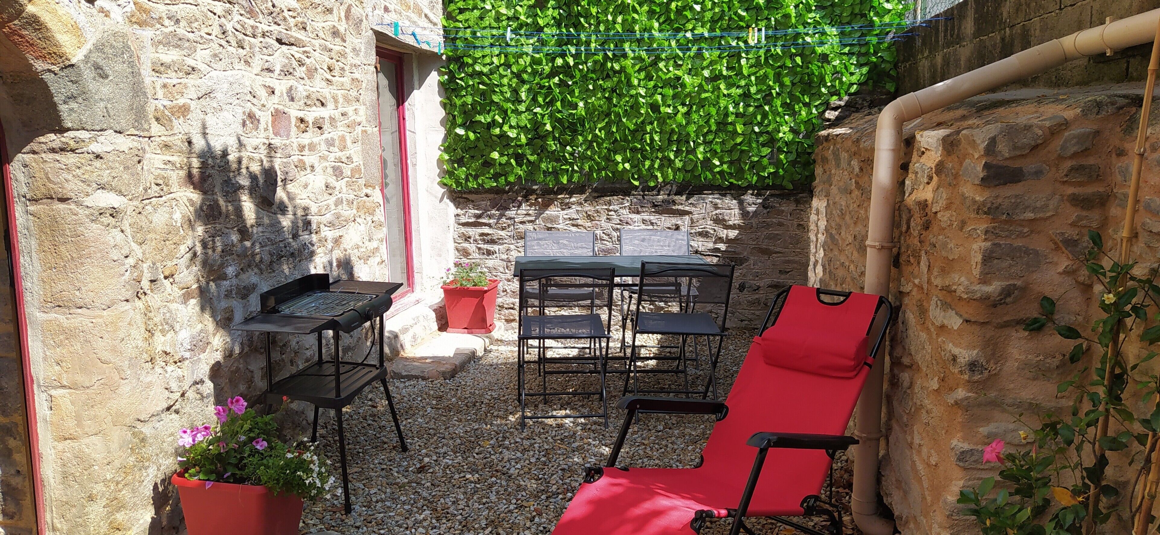 Un cortile in pietra con un tavolo e sedie, una sedia rossa e piante in vaso.