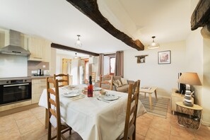 Un coin repas avec une table dressée pour quatre personnes, une cuisine équipée d’appareils modernes et un espace de vie chaleureux agrémenté d’une lampe et d’objets décoratifs.