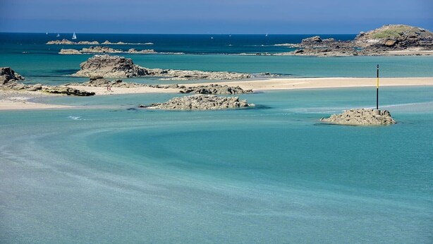 Paisatge costaner amb aigües turqueses cristal·lines, roques i una platja sorrenca.