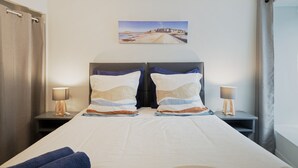 Habitació d'hotel amb un llit, dues taules de nit amb làmpades, un quadre a la paret i vista a la platja.