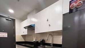 A modern kitchen with white cabinets, a black countertop, a stainless steel sink, and a black refrigerator. - W/ Secure Cabinets, complete appliance + Wifi (Davao City)