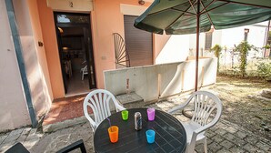 An outdoor patio with a round table, four chairs, and a green umbrella. - Cozy Apartment Near the Beach (Rosolina)