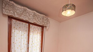A bedroom with two single beds, a nightstand, a lamp, and a window with curtains. - Cozy Apartment Near the Beach (Rosolina)