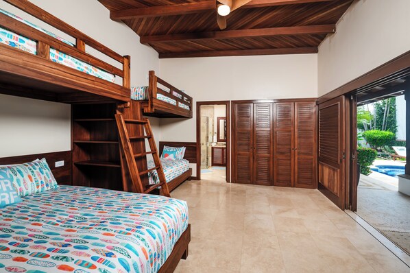 A bedroom with a bunk bed, a ladder, a wooden wardrobe, and a view of a swimming pool.