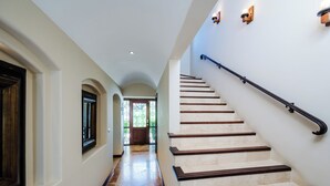 A hallway with a marble floor leading to a staircase with wooden steps and a black handrail.