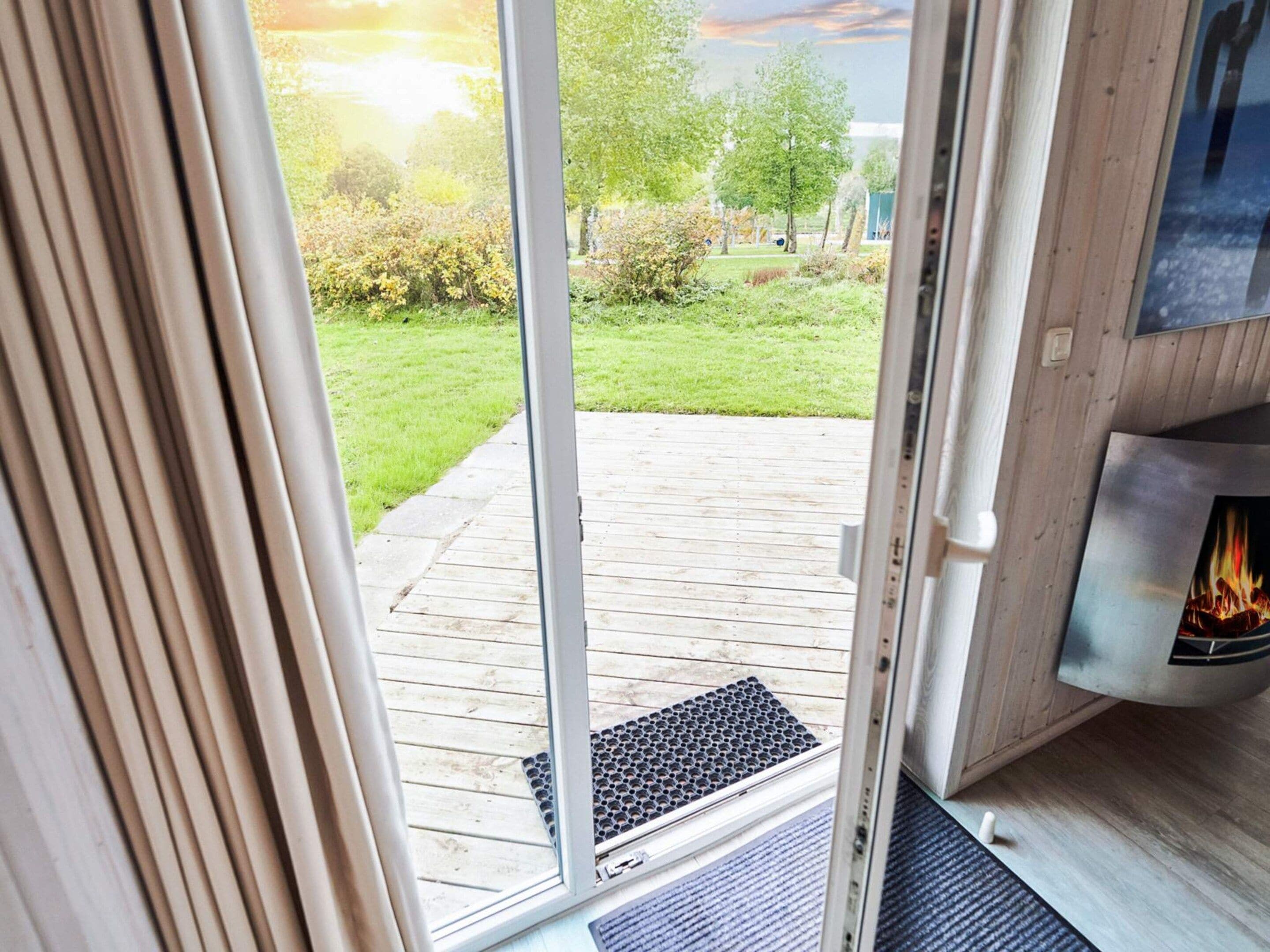 Eine Holzterrasse führt zu einer Glastür, hinter der ein Kaminfeuer sichtbar ist.
