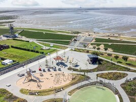 Vista aérea de un parque costero con áreas de juegos, campos deportivos y una zona de playa.