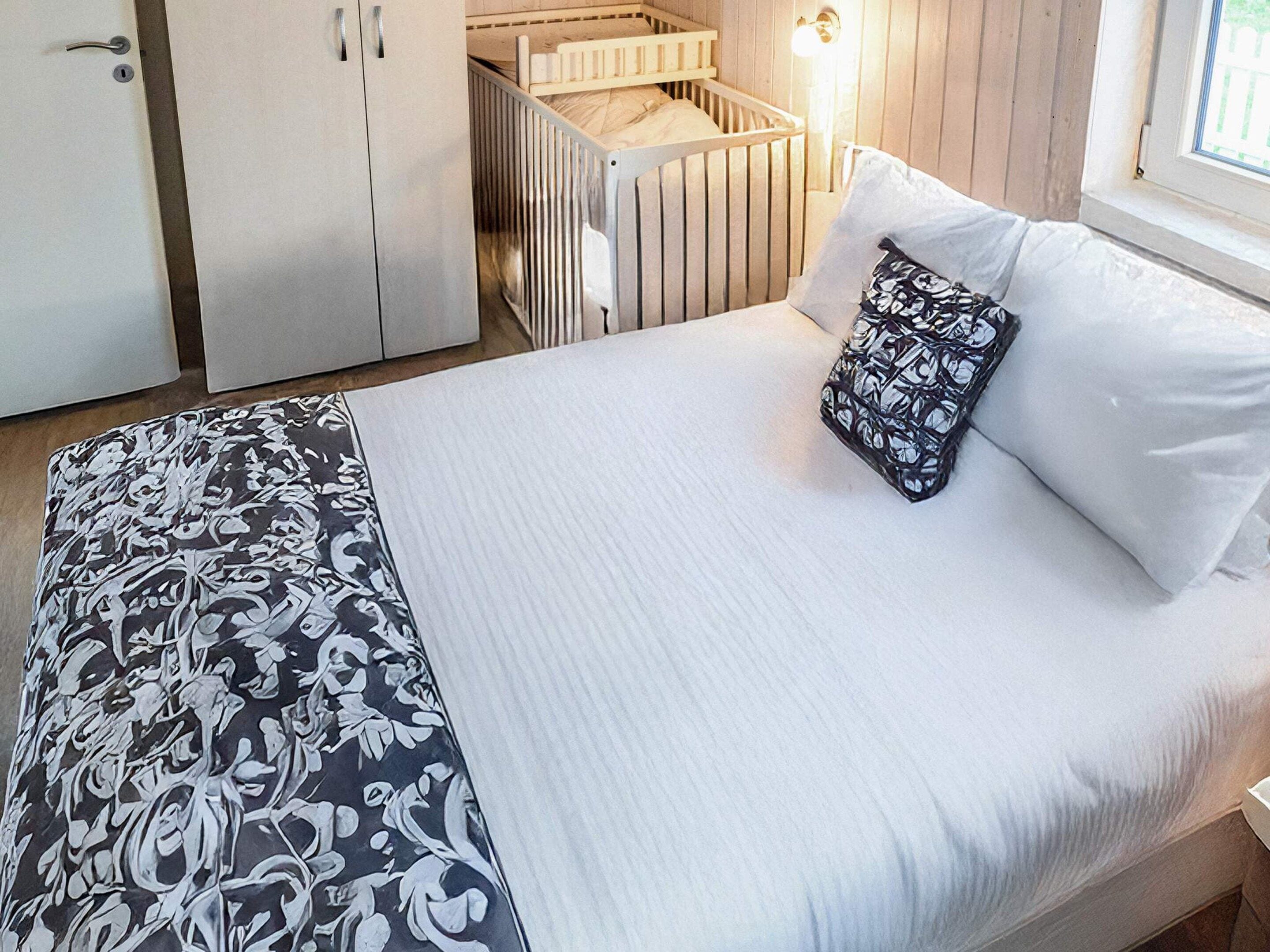 A bedroom with a bed, a crib, a wardrobe, and a window.