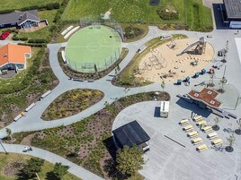 Vista aérea de un complejo deportivo con cancha de baloncesto, parque infantil y zona de estacionamiento.