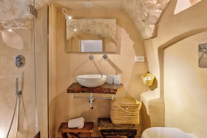 A bathroom with a glass shower enclosure, a white sink with a marble countertop, a mirror above the sink, and a woven basket on a wooden stool.