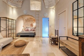A bedroom with a stone wall, a bed, a wooden bench, a ladder, and a door with a blue light.