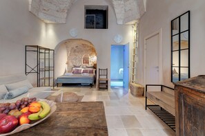 A cozy room with a bed, a wooden bench, a fruit basket, and a stone wall.