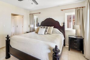 Quarto com uma cama grande, uma mesa de cabeceira, uma luminária e uma janela com cortinas.