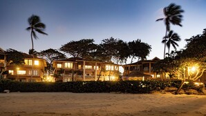 A beachfront hotel with multiple buildings, palm trees, and a well-lit facade.
