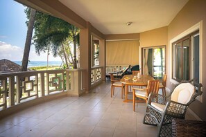 Uma varanda com mesa e cadeiras, uma cadeira de vime e vista para o mar.
