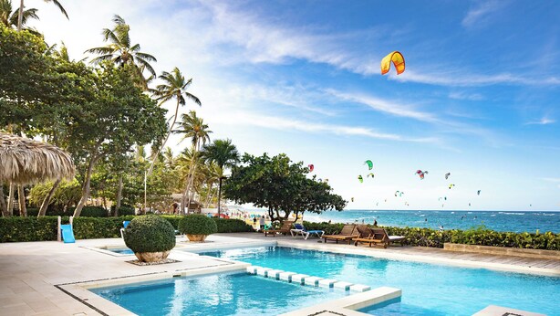 A pool area with a clear view of the ocean and people flying kites.
