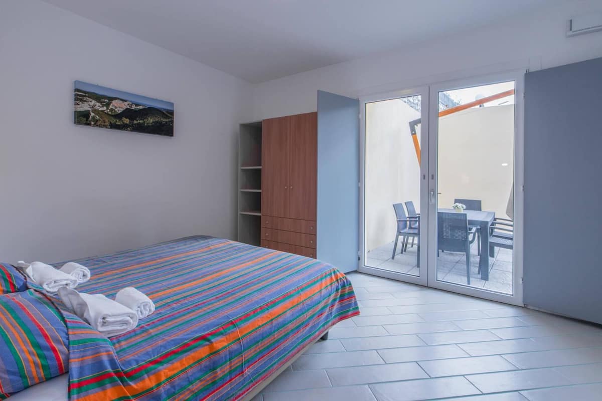 Ein Schlafzimmer mit Bett, Kleiderschrank und einer Schiebetür zu einem Sitzbereich im Freien.