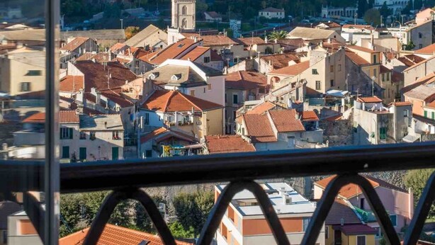 Un pueblo costero con una destacada torre de iglesia, edificios escalonados y montañas al fondo.