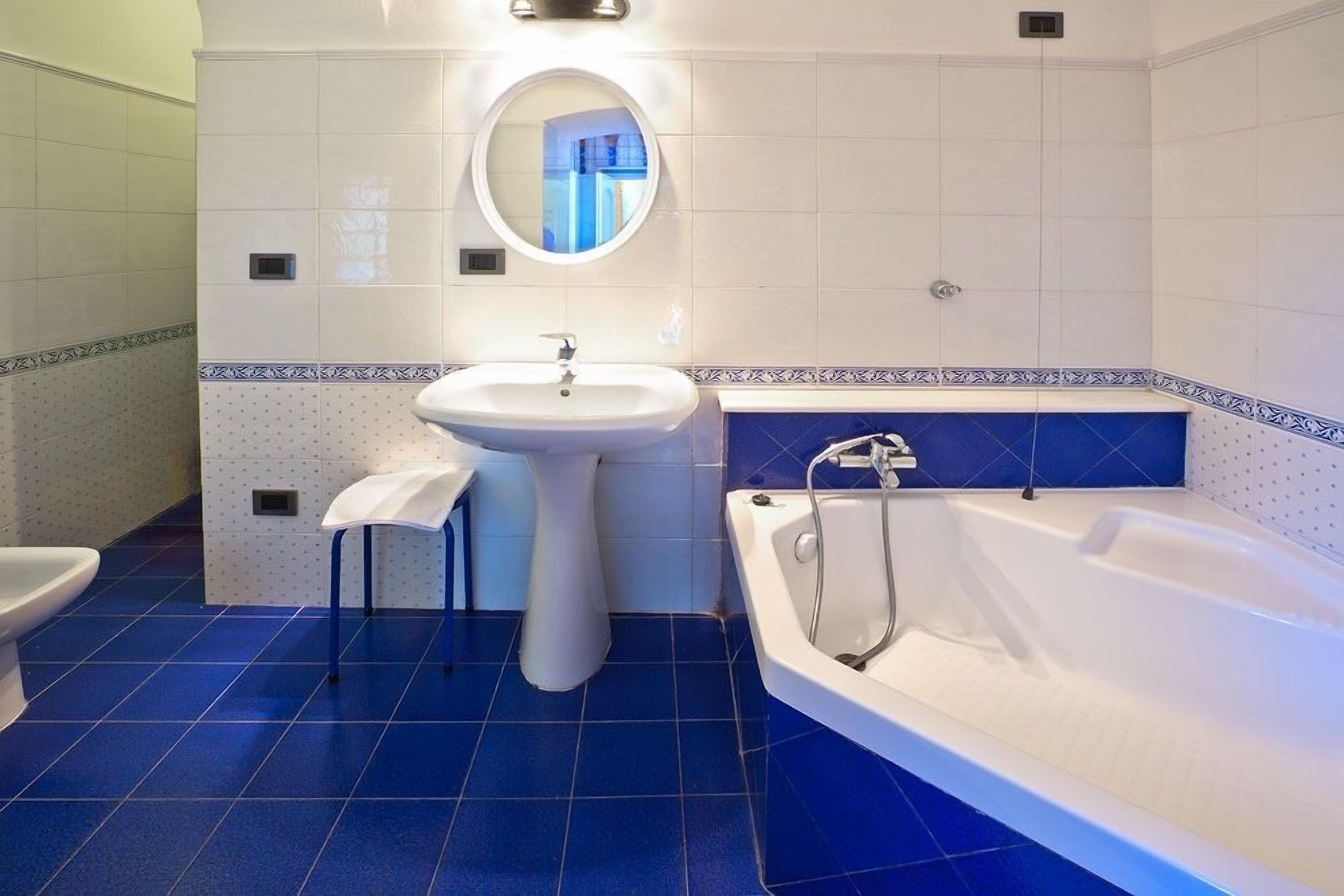 A bathroom with a white sink, a round mirror, a toilet, and a bathtub.