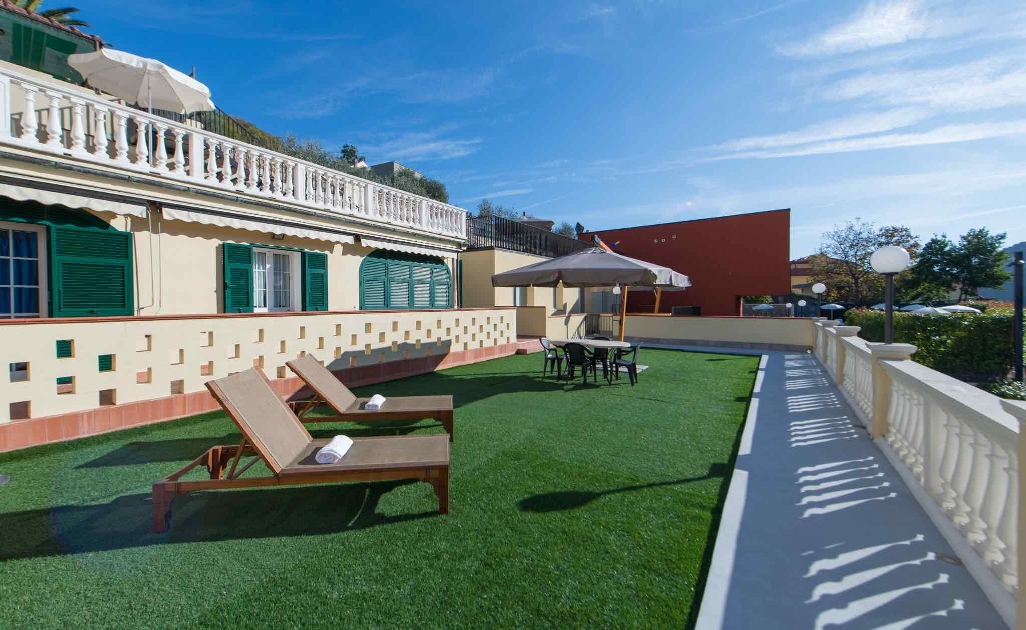 A rooftop terrace with artificial grass, lounge chairs, and a dining area.
