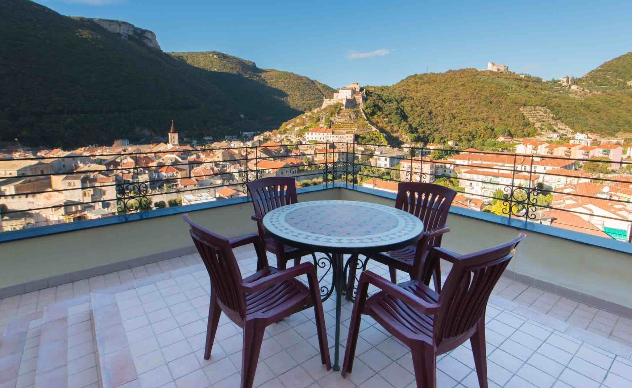 Une terrasse avec une table et des chaises, d’où l’on peut admirer une ville avec, au loin, une colline et un château.