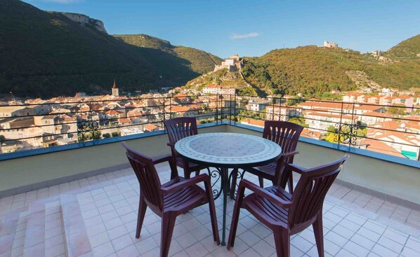 Una terraza con mesa y sillas que da a una vista de un pueblo con una colina y un castillo a lo lejos.