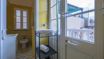 Une salle de bain avec des carreaux jaunes, des toilettes blanches, un lavabo et une fenêtre donnant sur un balcon.
