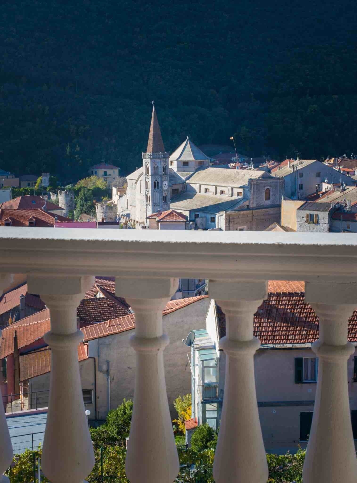 A balcony with a view of a town featuring historic buildings and a prominent church tower.