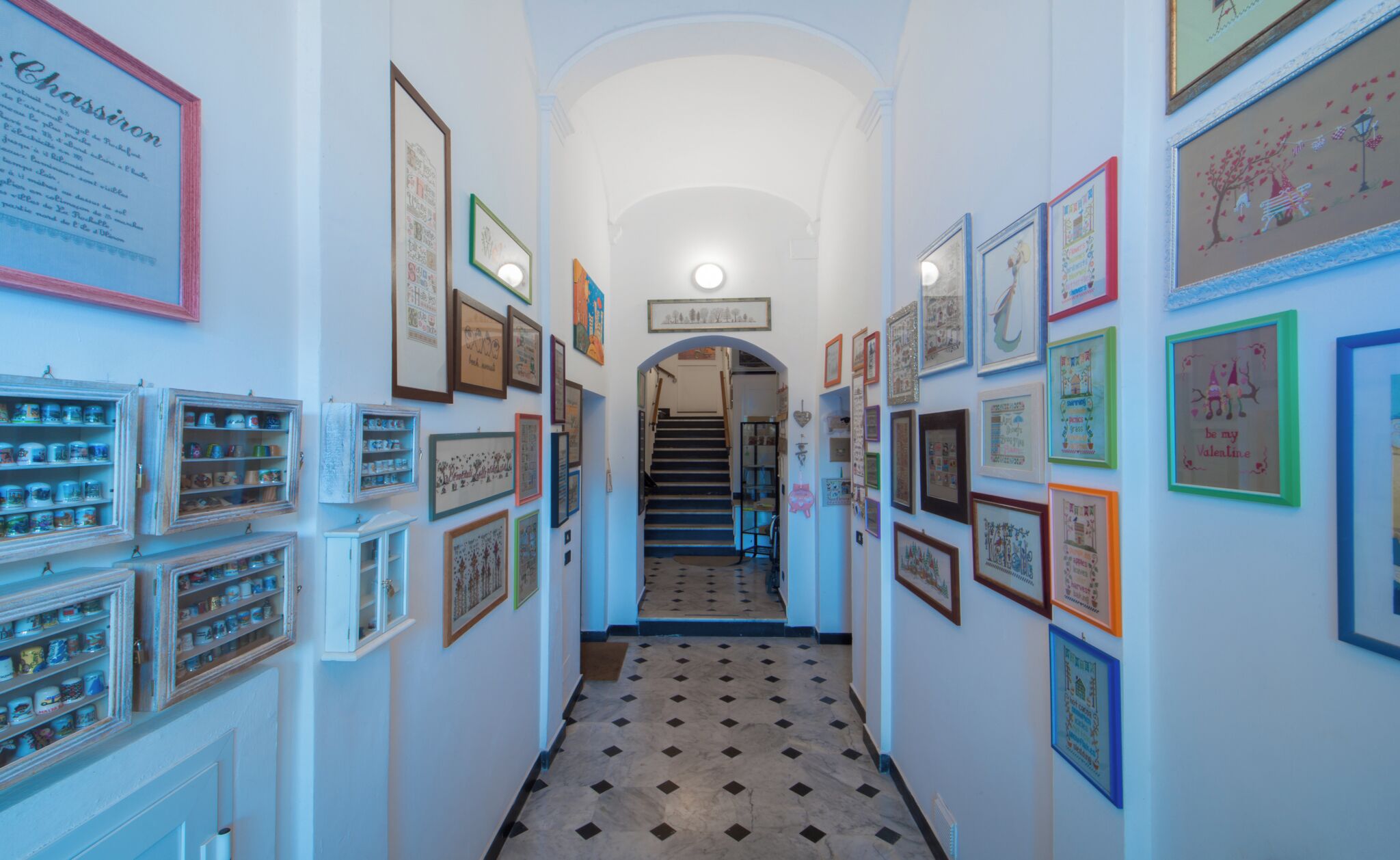 A hallway with framed pictures on the walls, a staircase, and a tiled floor.