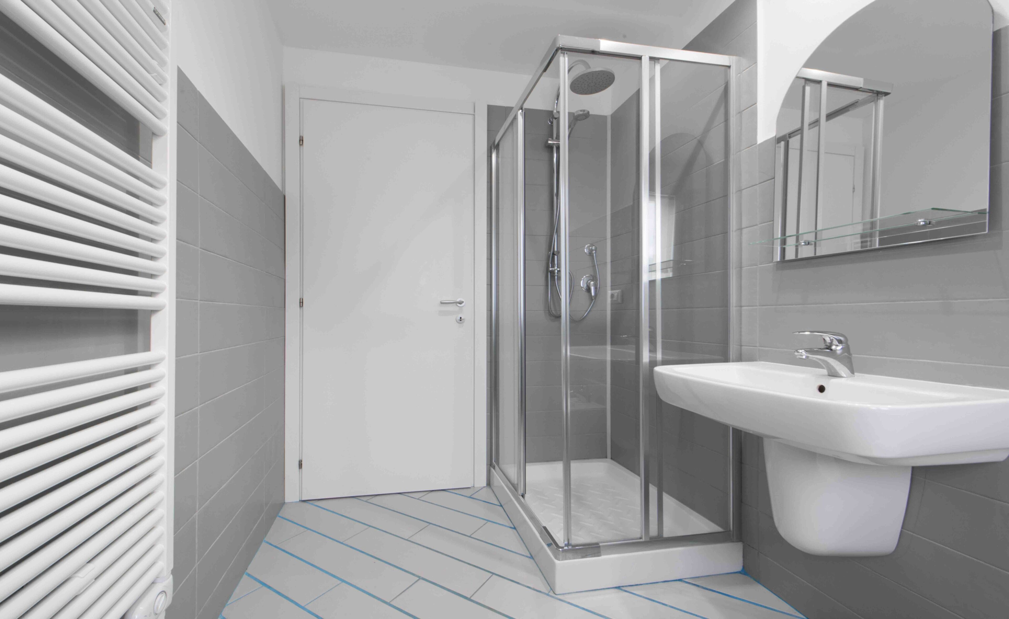 A modern bathroom with a glass-enclosed shower, a white sink, and a tiled floor.