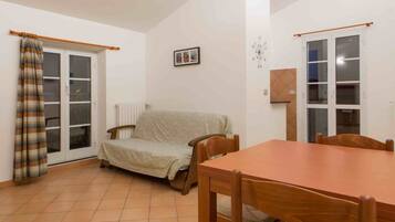 Una habitación con una mesa de comedor, un sofá, una ventana con cortinas y un radiador.
