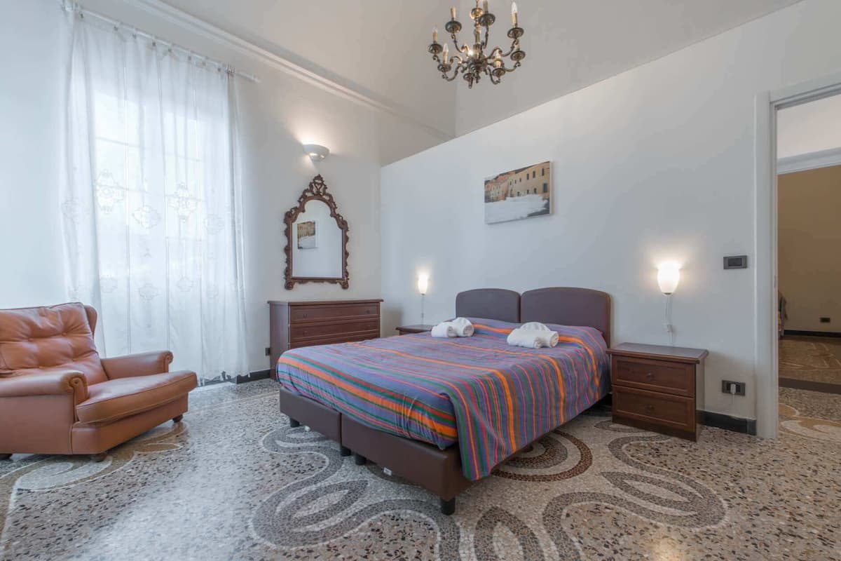 Ein Hotelzimmer mit Bett, Sessel, einer Kristallleuchtre, einem Gemälde und einer Tür.