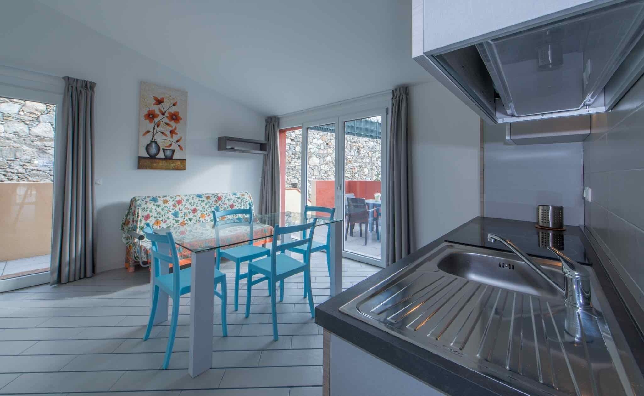 Een moderne keuken met een inbouwspoelbak en een eetgedeelte met een glazen tafel en blauwe stoelen.