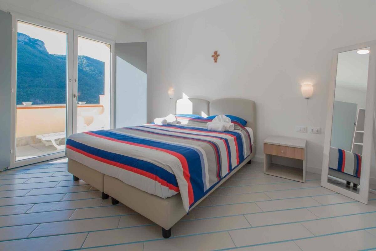 Ein Hotelzimmer mit Bett, Nachttisch, Spiegel und einem Balkon mit Bergblick.